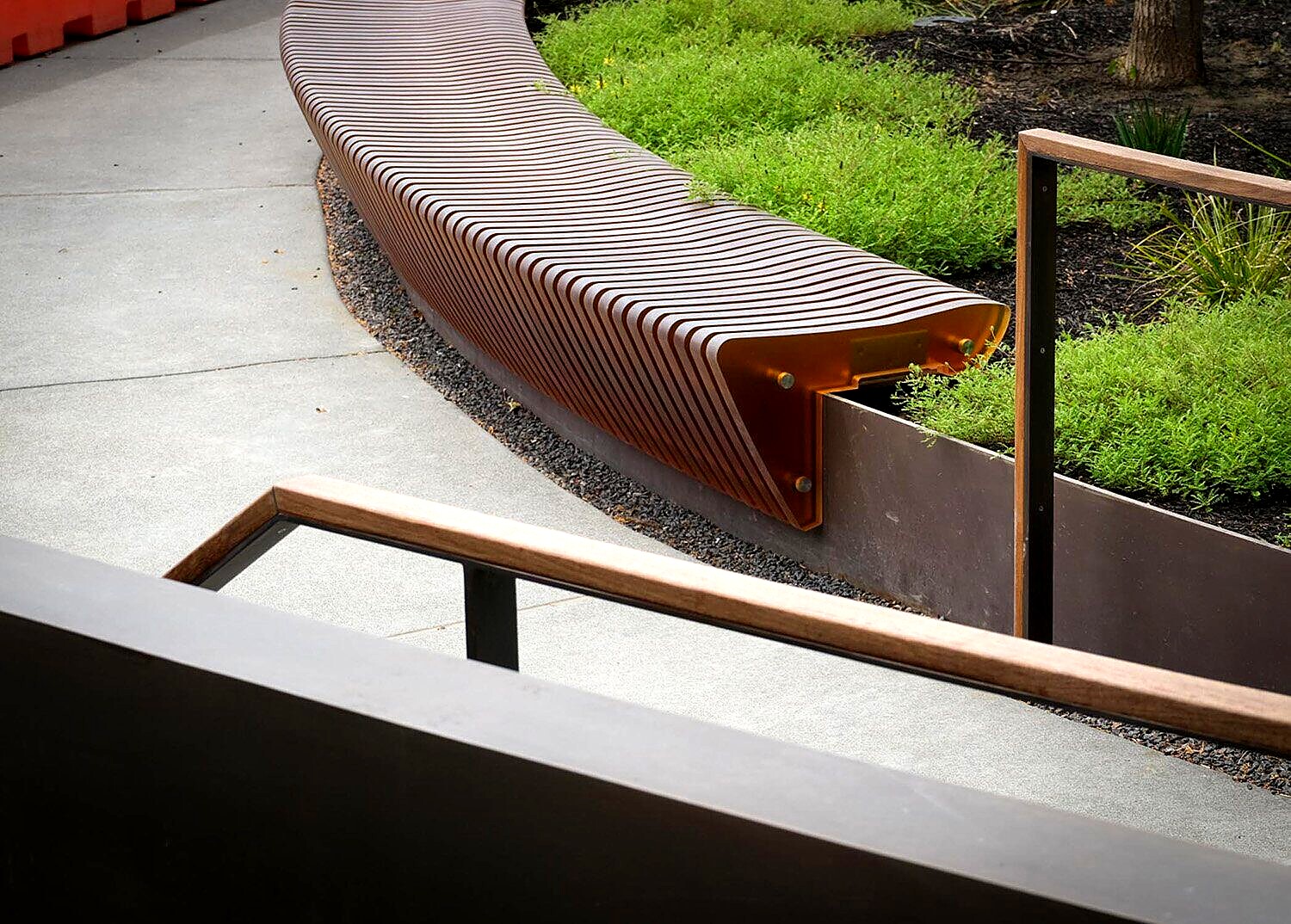 Cor-ten steel slat bench along a planter edge, wood-capped handrail