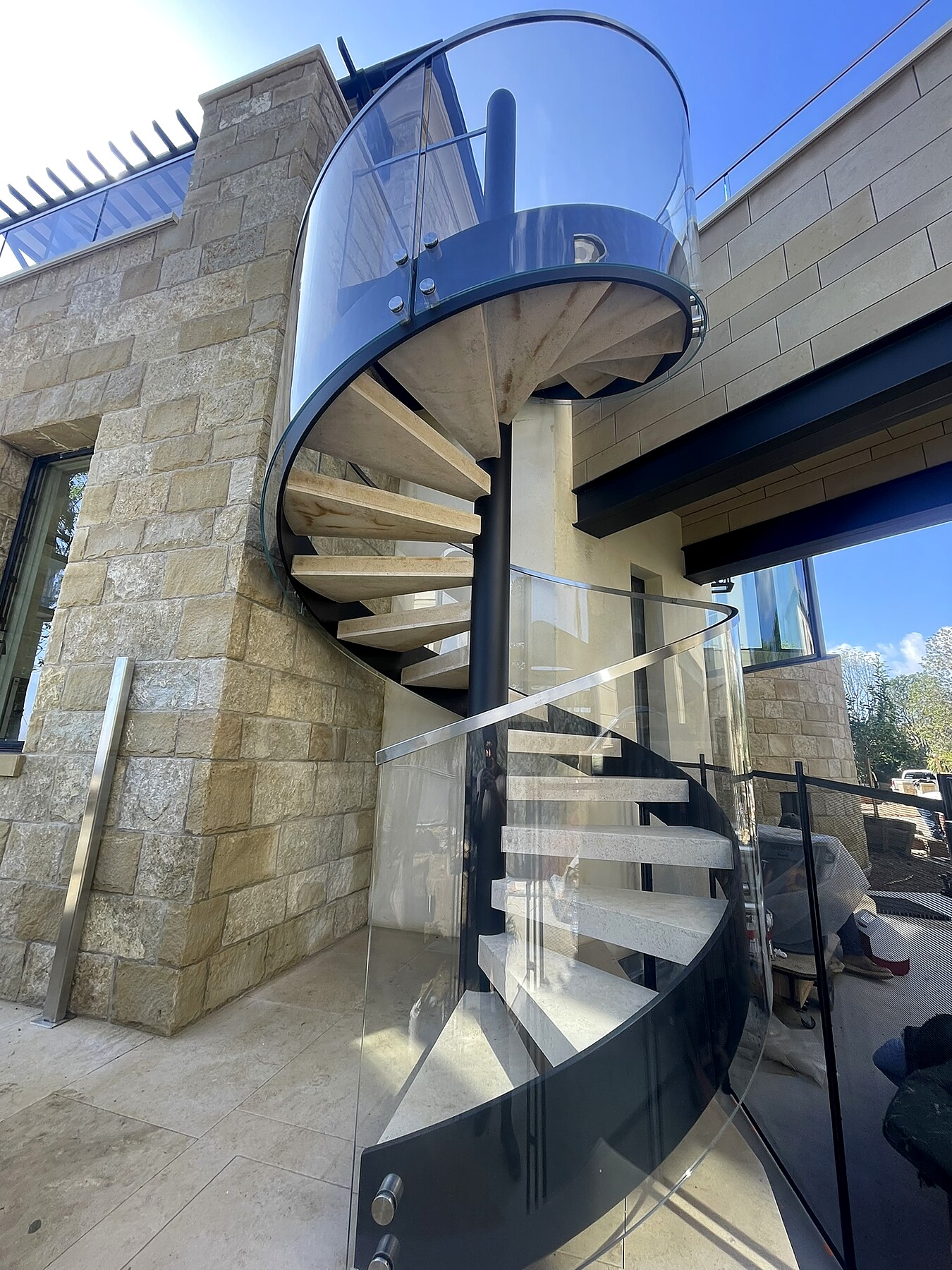 Glass-wrapped spiral staircase, exterior stone installation